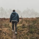man in black jacket and blue denim jeans standing on brown grass field during daytime
